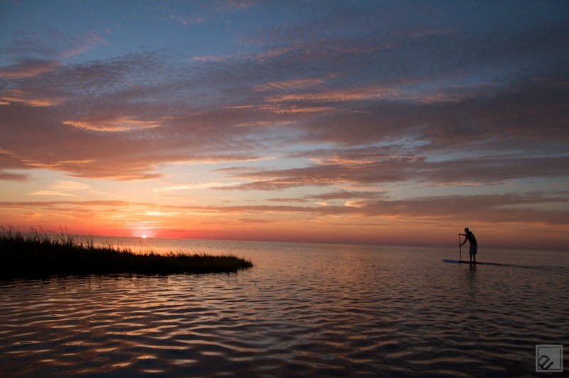 a standup paddleboarder paddles twords a sunset in cape hatteras nc a standup paddleboarder paddles twords a sunset in cape hatteras nc