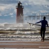 a surfer walks twords lake michigan and the rough waters by the south haven lighthouse