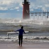 a surfer walks twords lake michigan and the rough waters by the south haven lighthouse